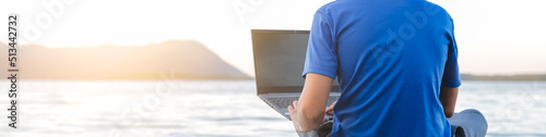 young hipster digital nomad man sitting on wooden pier at sea working on internet remotely at sunset - Traveling with a computer - Online dream job concept - Selective Focus.
