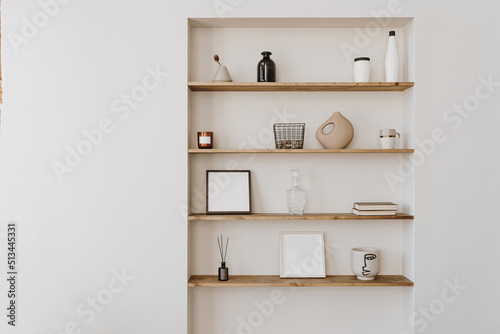 Decorated shelf on white wall. Aesthetic luxury minimalist home interior design decoration. Elegant Scandinavian, hygge style interior. Picture frames, fragrance, vase, books, candle