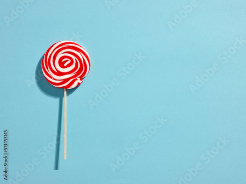 Red and white colored swirl round candy lollipop on blue background.