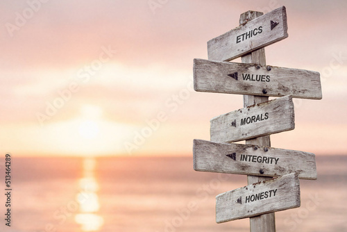 ethics values morals integrity honesty text engraved on wooden signpost at the beach during sunset.