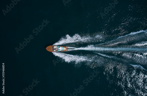 Modern wooden boat in a classic design, moving on water, aerial view. Luxurious wooden boat with people moves on dark water top view. Italian classic wooden boat fast movement on the water top view.