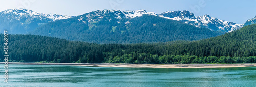 A panorama view of the densely forested shoreline in the Gastineau Channel on the approach to Juneau, Alaska in summertime