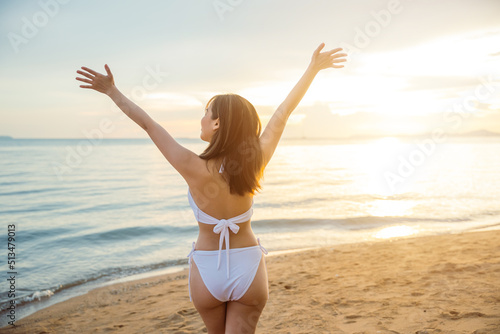 Back view. Happy young woman in bikini swimsuit posing relax in tropical sea beach with arms raised, Asian female raised hand up on summer holiday travel