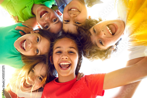 Bunch of cheerful joyful cute little children playing together and having fun. Group portrait of happy kids huddling, looking down at camera and smiling. Low angle, view from below. Friendship concept