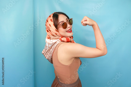 Retro concept of a young Asian strong woman showing her biceps isolated by a blue background
