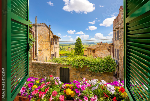 View through an open window with shutters out over the Tuscan countryside and medieval hilltop old town of San Gimignano, Italy.