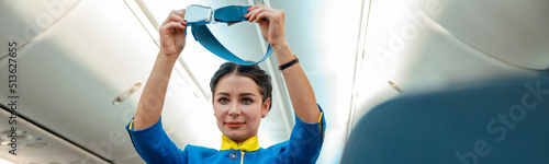 Female flight attendant in air hostess uniform holding seatbelt while standing near passenger seats in airplane