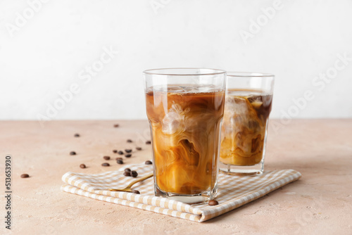 Glasses of cold brew coffee on beige table against light background
