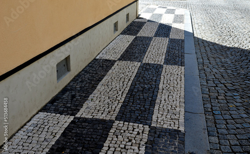 mosaic of small marble cubes. sidewalks and squares formed by stone carpet with squares, polka dots waves pattern. stone carpet pink, white dark background. basalt rough paving in space under tree