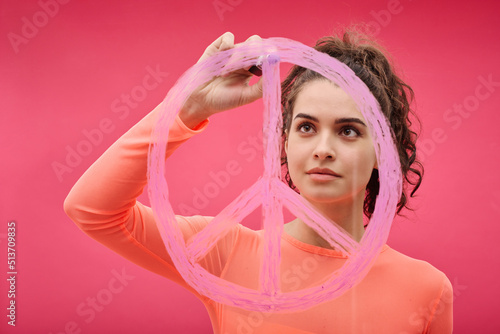 Young woman drawing pacifism sign with pink lipstick against color background