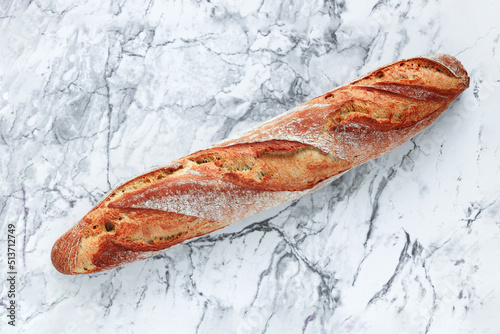 Rustic sourdough baguette on a marble table, top view. Free space for text