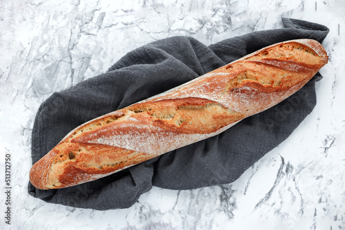 Fresh rustic french sourdough baguette on kitchen towel on marble table, top view. Free space for text