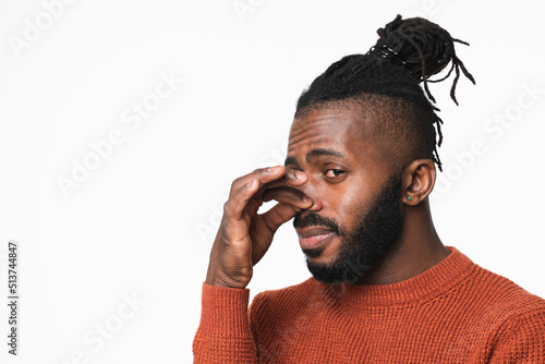 Young african-american man in red sweater with dreadlocks smelling stinky, closing nose with a hand because of odor stench isolated in white background