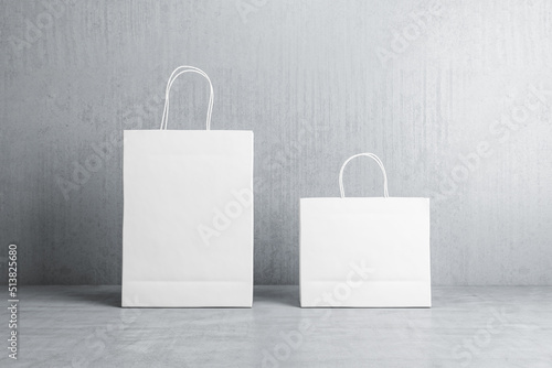 Front view on two blank white paper shopping bags with place for your logo or text on concrete floor on grey background. 3D rendering, mock up