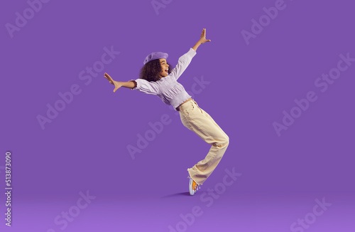 Cheerful joyful african american teenage girl having fun getting on her toes on purple background. Funny stylish preteen girl fooling around, rejoicing and laughing out loud. Full height. Banner.