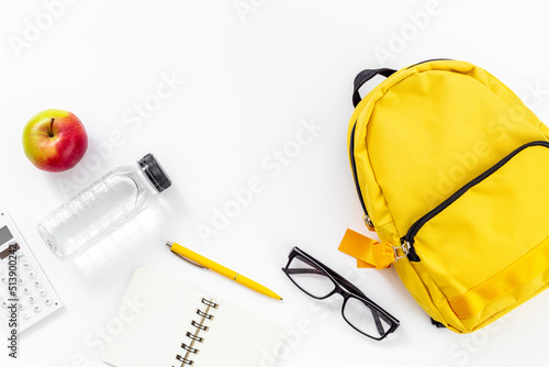 Back to school concept. Yellow school backpack with supplies water and apple