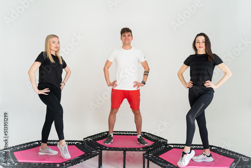 Three adorable fitness people In sportswear jumping on sport trampoline White background