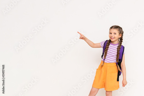 A child with a satchel points with his index finger at your advertisement on a white isolated background. Preparatory summer courses for children. Copy space.