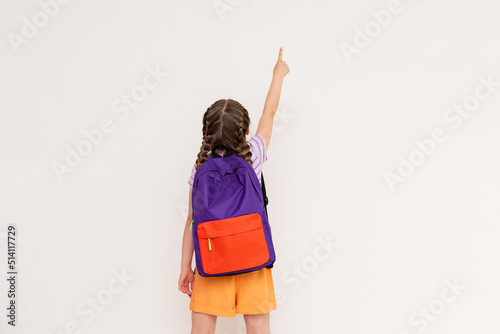 A child with a satchel points with his index finger at your advertisement on a white isolated background. Preparatory summer courses for children.