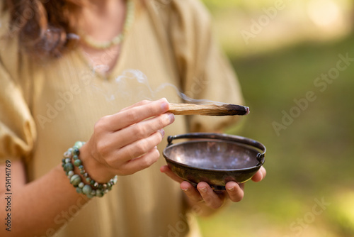 occult science and supernatural concept - close up of woman or witch with smoking palo santo stick and bowl performing magic ritual in forest