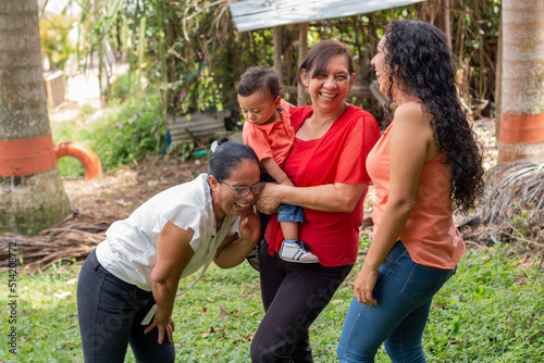 Three latin women socializing and laughing together in a nature park, and a latin baby in his grandmother's arms.