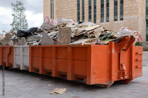 huge heap on metal Big Overloaded dumpster waste container filled with construction waste, drywall and other rubble near a construction site.