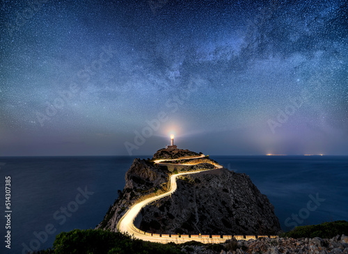 Night time image with milky way stars and illuminated road with light trails at the Far de Formentor lighthouse on Mallorca, Spain