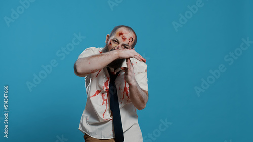Frightening evil looking zombie making timeout hand gesture on blue background. Scary mindless brain-eating apocalyptic monster doing break time hand signal while looking at camera. Studio shot