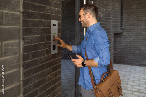 Smiling businessman using intercom while standing at building entrance in the city