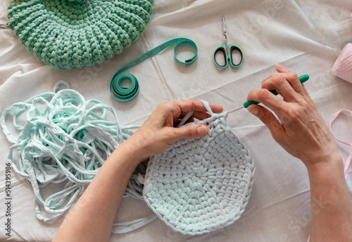Women's hands crocheting a bag from knitted yarn. Flatley from scissors, centimeter, hook, yarn. The concept of creating a bag from knitted yarn.