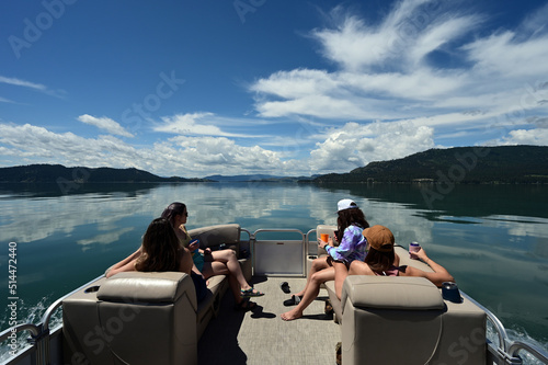 Four young women enjoying ride on pontoon boat on calm water of Flathead Lake, Montana on sunny summer morning.