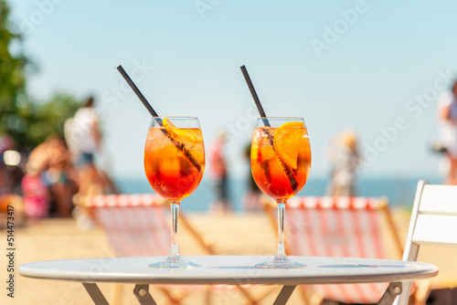 Two glasses of orange spritz aperol drink cocktail on table outdoors with sea and trees view blurred background.