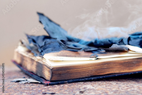 An open book with burnt charred pages and smoke on the table. Burning of banned literature