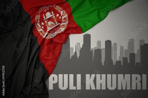 abstract silhouette of the city with text Puli Khumri near waving national flag of afghanistan on a gray background.