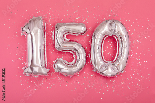 Silver balloon number 150 one hundred fifty shape sparkles scattered randomly on juicy pink background. Silver confetti pink background