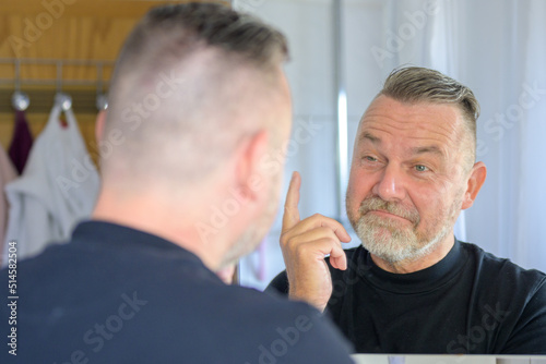 Senior man looking at his reflection with a rueful smile
