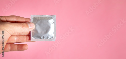 Male hand showing condom on pink background.