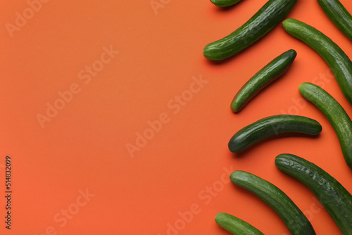 Fresh ripe cucumbers on orange background, flat lay. Space for text