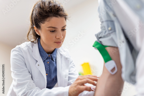 Friendly hospital phlebotomist collecting blood sample from patient in lab. Preparation for blood test by female doctor medical uniform on the table in white bright room