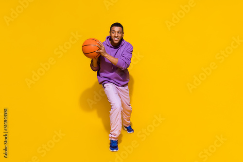 Full length body size view of attractive cheery sportive guy playing basketball isolated over vivid yellow color background