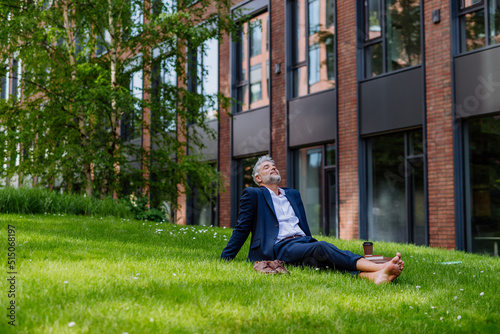 Mature businessman resting and sitting barefoot in park, feeling free, escaping from work, work life balance concept.