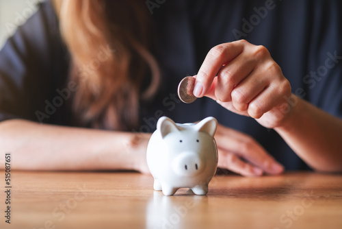 Closeup image of a woman putting coin into piggy bank for saving money concept