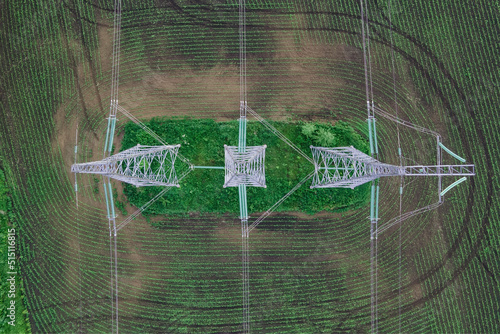 High voltage electric power tower in a green agricultural landscape aerial top view