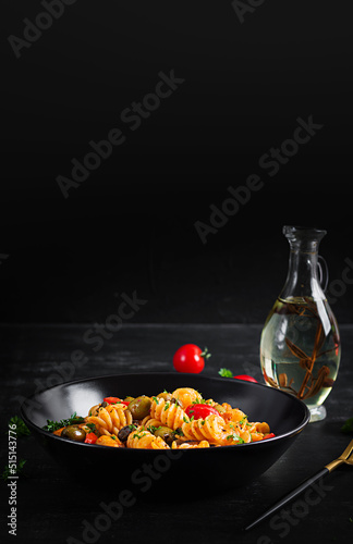 Classic italian pasta fusilli marinara with mussels, green olives and capers on dark table. Fusilli pasta with sauce marinara