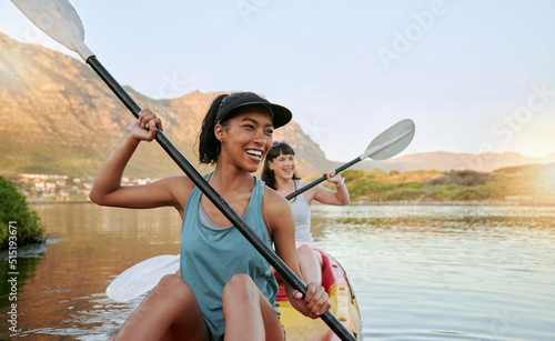 Two smiling friends kayaking on a lake together during summer break. Smiling and happy playful women bonding outside in nature with water activity. Having fun on a kayak during weekend recreation