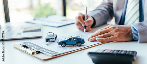 Man signing car insurance document or lease paper. Writing signature on contract or agreement. Buying or selling new or used vehicle. Car keys on table. Warranty or guarantee. Customer or salesman.