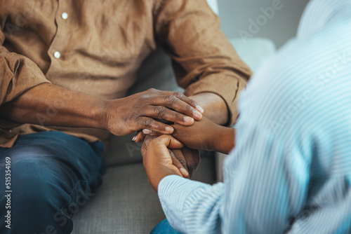 Close up black woman and man sitting on couch two people holding hands. Symbol sign sincere feelings, compassion, loved one, say sorry. Reliable person, trusted friend, true friendship concept