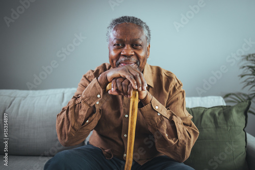 Shot of a senior man looking thoughtfully out of a window at home. Positive African American senior grandfather with grey hair and beard sitting at home. Elderly man sitting alone at home