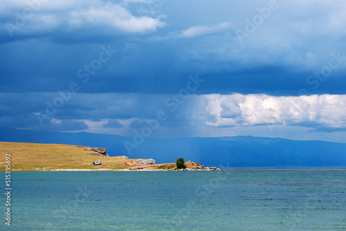 Distant cape with a lone tree and rainy cloud above.