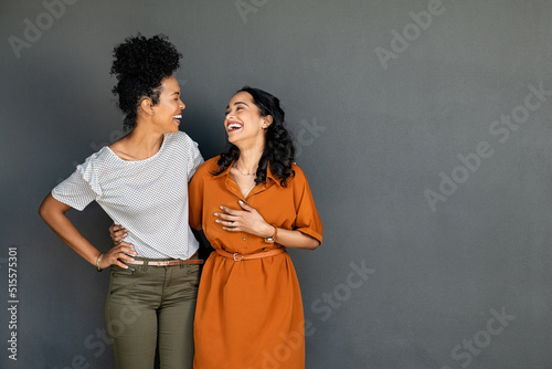 Two women friends embracing and laughing on grey background